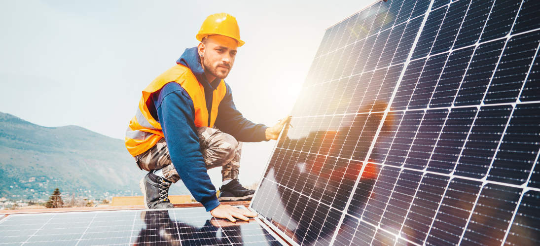 A man in a hard hat and orange vest installing a solar panel